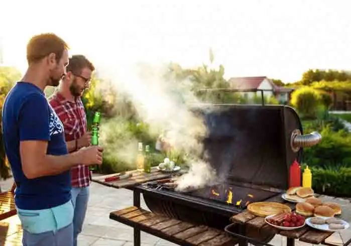 To mænd der hygger sig ved en grill og drikker øl